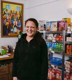 A smiling woman standing in front of a full pantry of donated food products